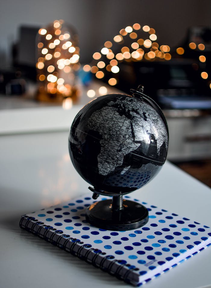 creative-approach-img Elegant black globe and notebook against warm bokeh lights, perfect for educational themes.