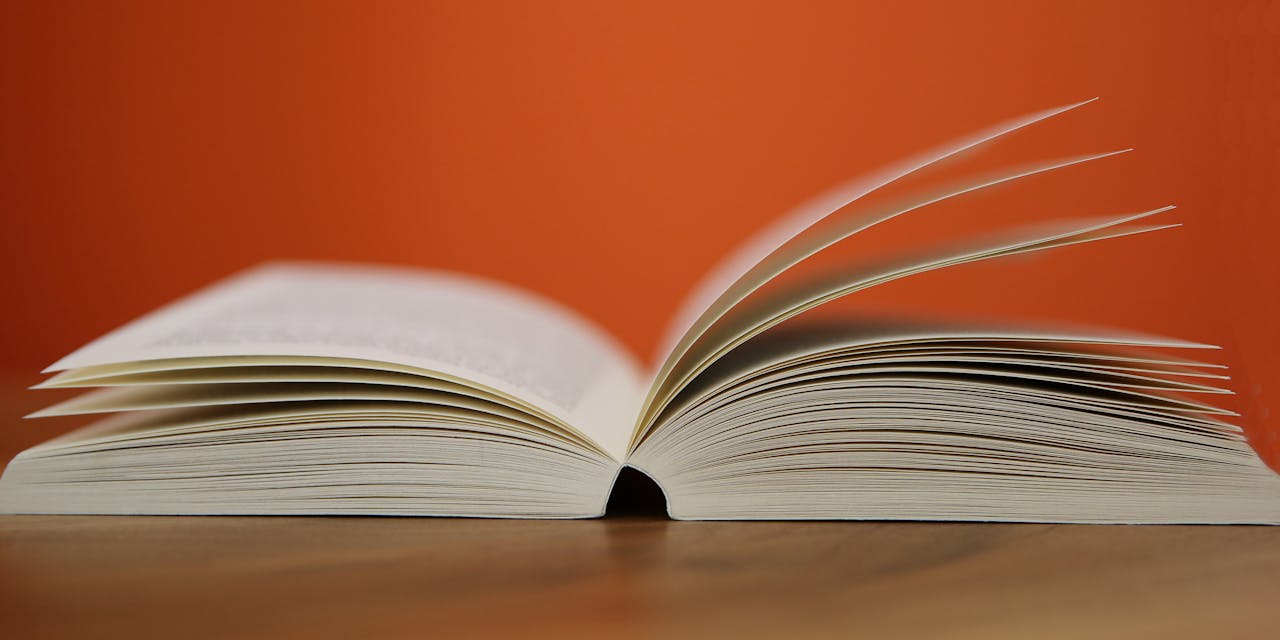 Mastering the First Impression: Your intriguing post title goes here An open book with pages turning against a vibrant orange background, symbolizing knowledge and education.