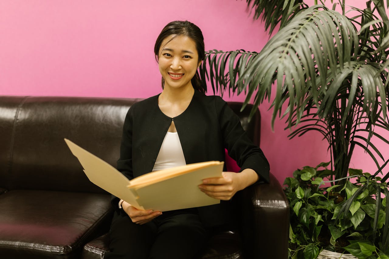 Young woman in business attire holding a folder on a couch with vibrant background.