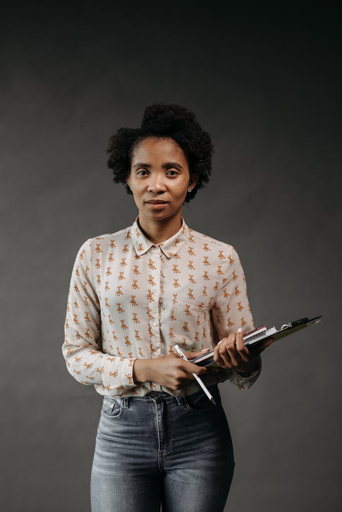 Portrait of a confident teacher with afro hair holding a clipboard in a studio setting.
